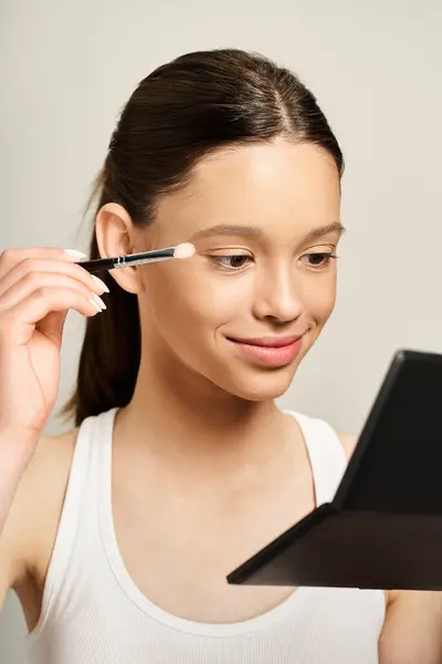 Une adolescente élégante utilisant énergiquement un pinceau pour appliquer le maquillage sur son propre visage, mettant en valeur une forme amusante et artistique de l'expression de soi. — Photo de stock