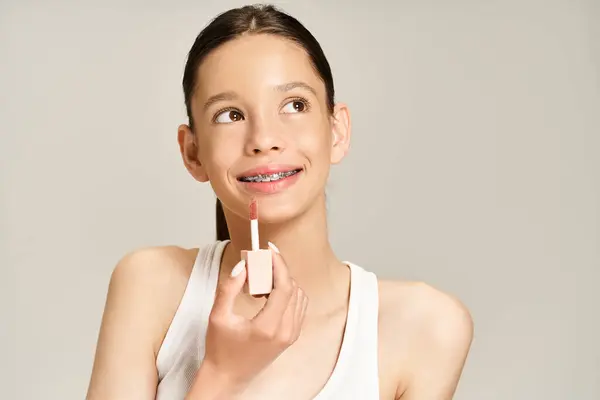 Ein stilvolles Teenager-Mädchen in lebendiger Kleidung hält sich spielerisch einen Lippenbalsam vor das Gesicht und versprüht Charisma und Charme. — Stockfoto