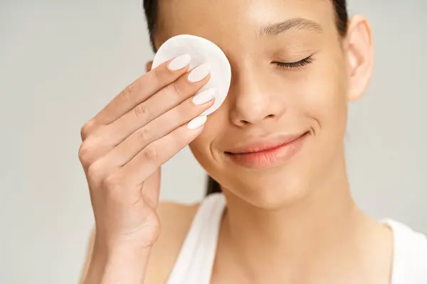 A stylish, vibrant teenage girl holds up cotton pad, looking through it with curiosity and wonder. — Stock Photo