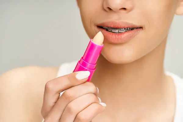 Una adolescente con estilo en traje vibrante sostiene un lápiz labial rosa, exudando confianza y glamour. - foto de stock
