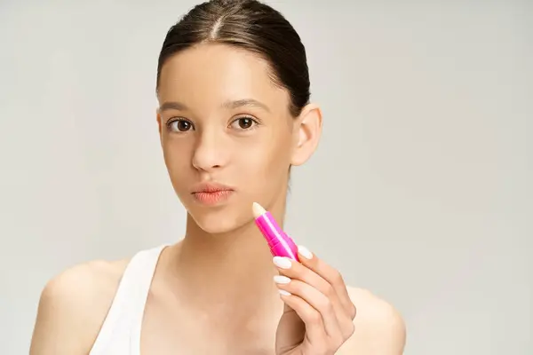 Elegante adolescente en ropa de moda tiene un lápiz labial rosa en la mano. - foto de stock
