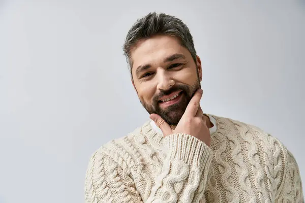 Ein bezaubernder Mann mit Bart posiert im weißen Pullover vor grauer Studiokulisse. — Stockfoto