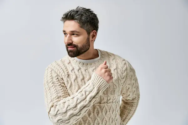 A charismatic man with a beard strikes a pose in a white sweater against a grey studio backdrop. — Stock Photo
