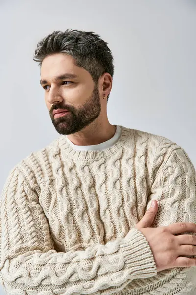 A fashionable man with a beard strikes a pose in a white sweater against a grey studio background. — Stock Photo