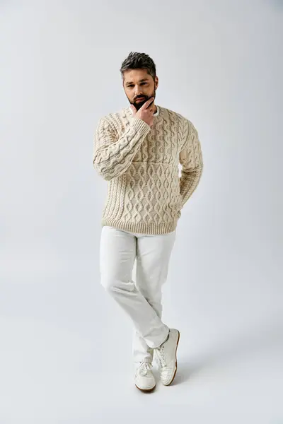 Ein bärtiger Mann posiert anmutig im weißen Pullover vor grauer Studiokulisse. — Stockfoto