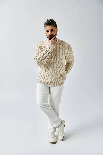 A bearded man poses gracefully in a white sweater against a grey studio backdrop. — Stock Photo