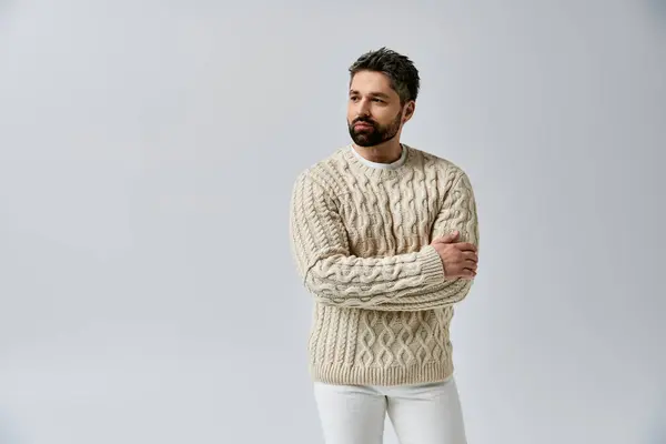 Ein stilvoller Mann mit Bart posiert im weißen Pullover vor grauer Studiokulisse. — Stockfoto