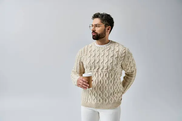 Ein bärtiger Mann versprüht Charme in einem weißen Pullover vor grauem Hintergrund und präsentiert einen raffinierten und polierten Look. — Stockfoto