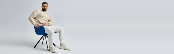 A bearded man in a white sweater sits gracefully in a chair, exuding an air of contemplation and sophistication. — Stock Photo