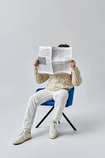 Чоловік, одягнений у білий светр, сидить у кріслі, інтенсивно зосереджений на читанні газети. — стокове фото