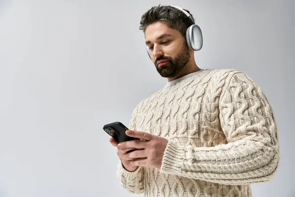 A bearded man wearing headphones gazes at his phone, lost in the music playing through his headset. — Stock Photo