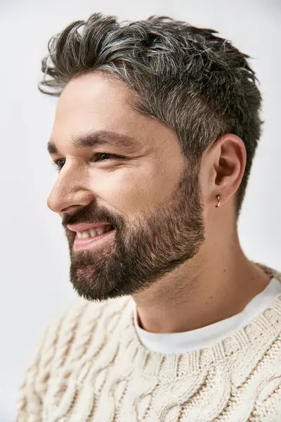 A captivating man with a beard strikes a pose in a cozy white sweater against a grey studio backdrop. — Stock Photo