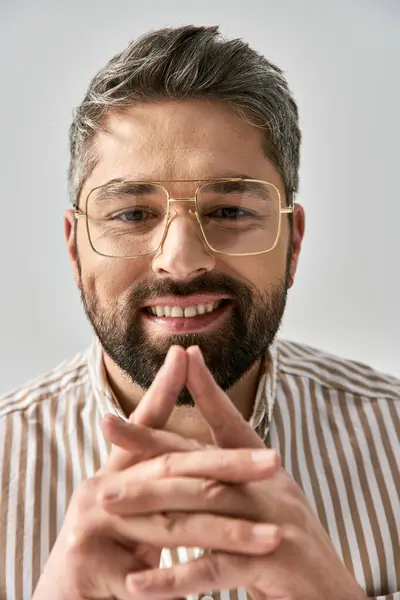 Um homem barbudo de óculos e uma camisa listrada posa elegantemente em um fundo cinza em um estúdio. — Fotografia de Stock