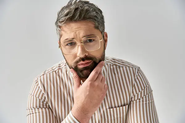 A stylish man with glasses gazes confidently at the camera in elegant attire against a grey studio backdrop. — Stock Photo