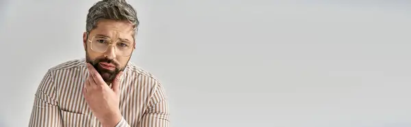 A stylish man with a beard and elegant attire looks surprised in a studio setting against a grey background. — Stock Photo