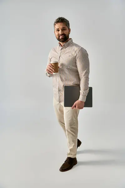 A bearded man in elegant attire holding a laptop and a cup of coffee, exuding sophistication and relaxation. — Stock Photo