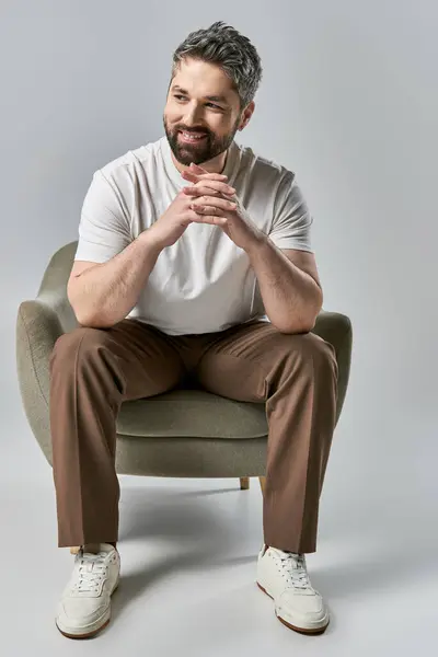 A stylish man with a beard sits on a chair with folded hands, exuding a sense of tranquility and deep thought. — Stock Photo