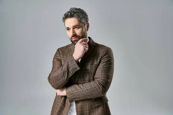 A bearded man poses elegantly in a brown jacket against a grey background in a studio setting. — Stock Photo