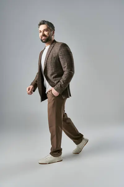 A stylish man with a beard in an elegant brown suit and white shirt striking a pose against a grey studio backdrop. — Stock Photo