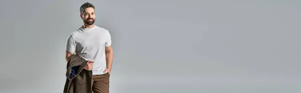 Um homem na moda com uma barba faz uma pose em traje elegante, em pé na frente de uma parede branca nítida. — Fotografia de Stock