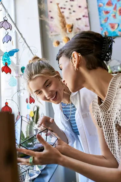 Two women in an art studio, engrossed in viewing a cell phone together. — Stock Photo