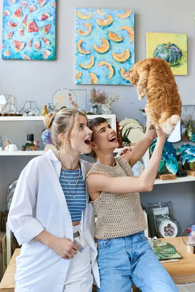 Two women hold a cat up to their faces, showing love and affection at an art studio. — Stock Photo