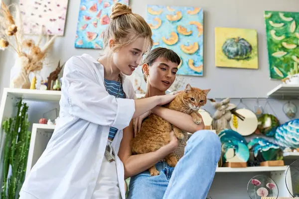 Two women holding a cat in her arms, surrounded by art supplies in a studio. — Stock Photo