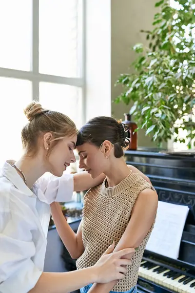Due donne, una coppia lesbica amorevole, in piedi con grazia accanto a un pianoforte in uno studio d'arte. — Foto stock