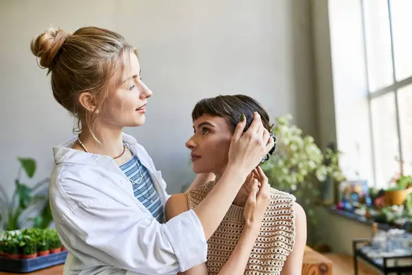 A woman lovingly styles another womans hair in an art studio. — Stock Photo