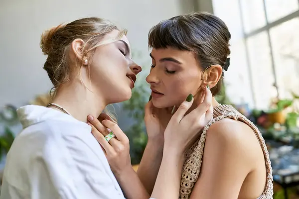 Two arty women stand together by window, sharing a tender moment. — Stock Photo
