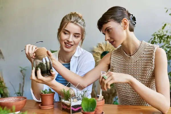 Dos mujeres admirando una planta en maceta juntas en un estudio de arte. - foto de stock