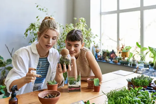 Arty lesbian couple enjoying time together surrounded by greenery at a table. - foto de stock