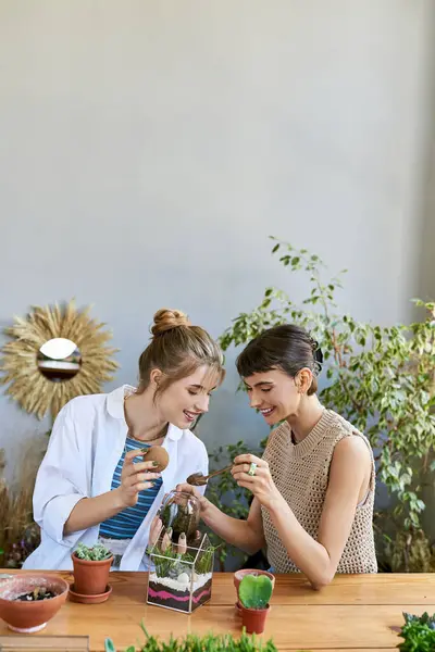 Две женщины, разделяющие момент за столом, окружённые растениями в художественной студии. — стоковое фото
