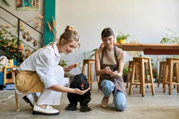 Two women kneels lovingly next to a black hen in an art studio. — Stock Photo