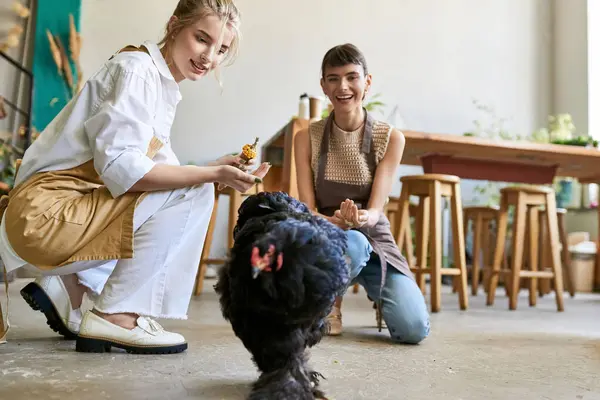 Zwei Frauen interagieren in einem Kunstatelier zärtlich mit einer schwarzen Henne. — Stockfoto