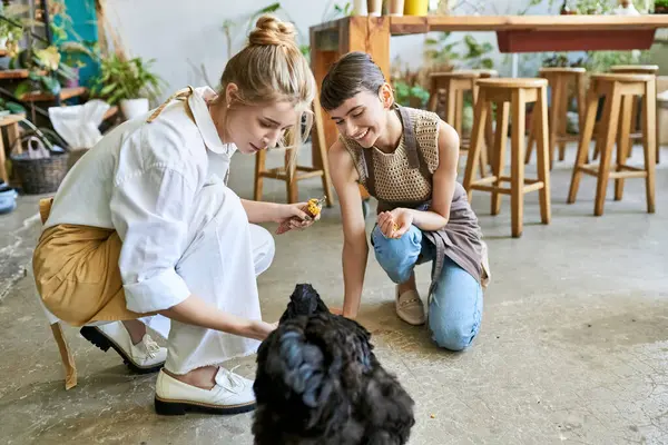 Loving lesbian couple petting a black hen on the floor in their art studio. — Stock Photo
