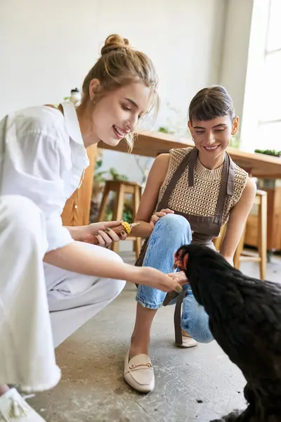 A woman lovingly pets a chicken while another woman looks on tenderly in an art studio. — Stock Photo