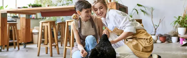 Two women in an art studio showing affection to a black hen. — Stock Photo