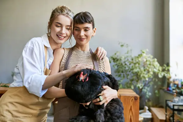 Two women in tender embrace with hen at an art studio. — Stock Photo