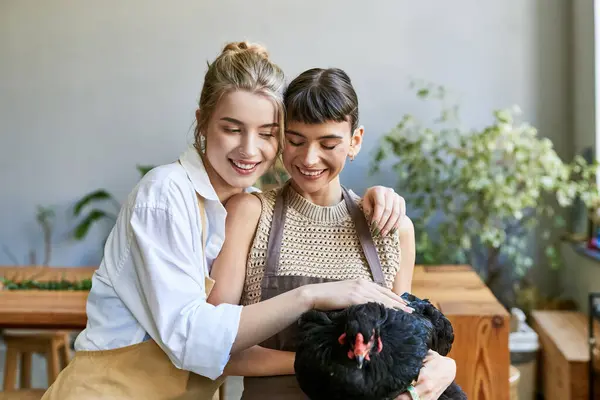 Two women at an art studio, one holding a black chicken tenderly. — Stock Photo