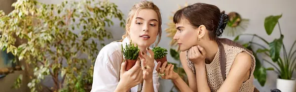 Lesbian couple enjoying art studio, holding plants, surrounded by creativity. — Stock Photo
