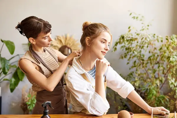 Two women standing at a table with a plant, displaying a nurturing and artistic connection. — Stock Photo