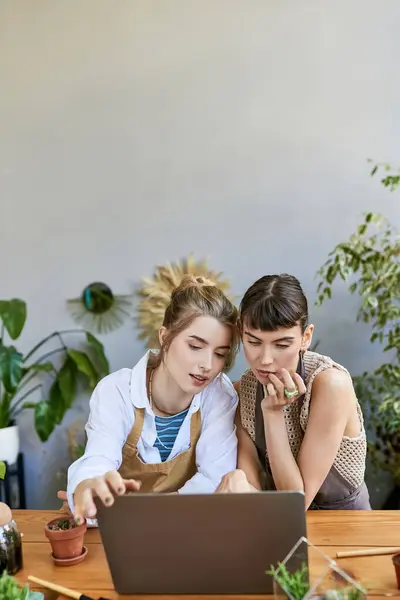Una coppia lesbica amorevole immersa nella loro arte, collaborando su un computer portatile a un tavolo. — Foto stock