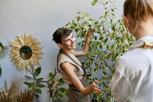 Lesbian couple in an art studio, one woman standing next to another holding a plant. — Stock Photo