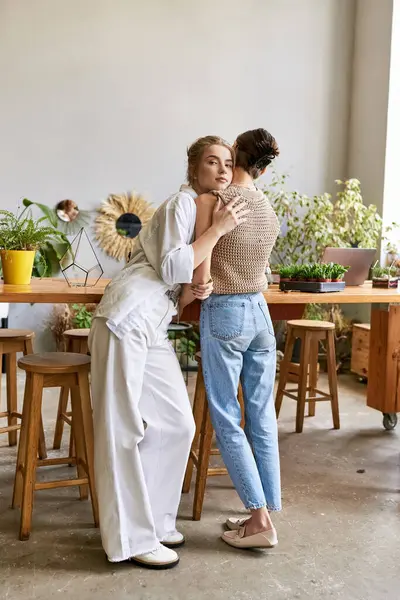 Two women, a loving lesbian couple, stand together near an art studio table. — Stock Photo
