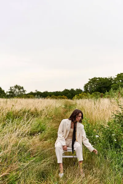 Молодая женщина в белом, сидящая на стуле в спокойном поле, купающаяся в теплом летнем бризе. — стоковое фото