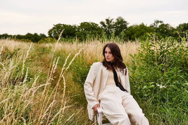 Красивая молодая женщина в белой одежде мирно сидит на стуле в поле, впитывая летний бриз.. — стоковое фото