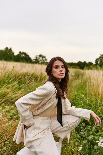 Eine schöne junge Frau in weißem Anzug und Krawatte steht anmutig auf einem Feld und genießt die Sommerbrise. — Stockfoto