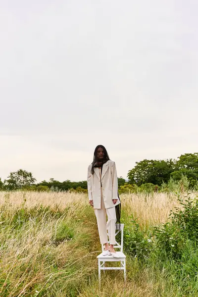 Красивая молодая женщина в белом стоит на стуле в ярком поле, обнимая летний бриз. — стоковое фото