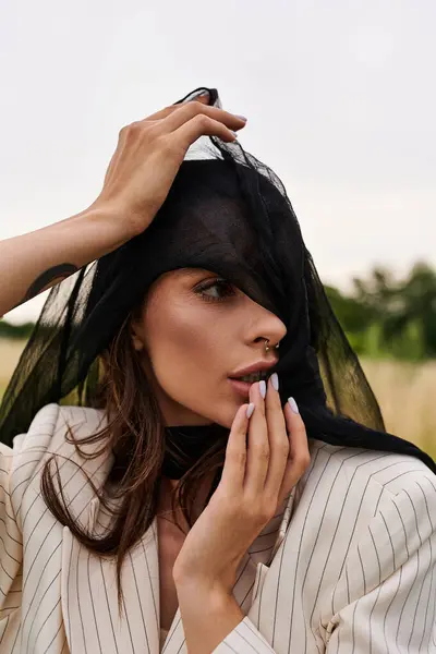 Uma jovem mulher de traje branco desfrutando da brisa de verão em um campo, sua cabeça adornada com um véu delicado. — Fotografia de Stock